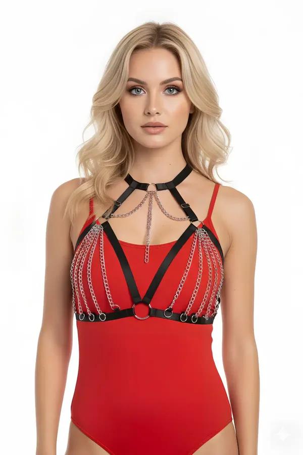 Black faux leather chest harness with cascading silver chain rows and O-ring hardware worn over red bodysuit
