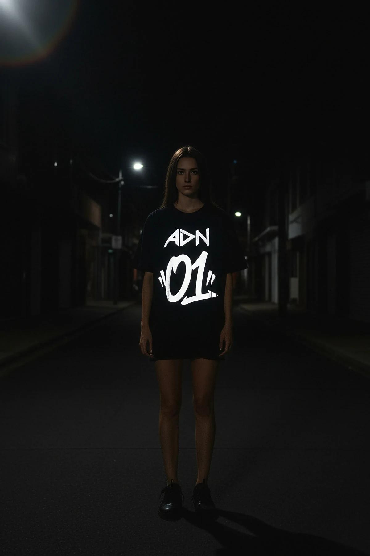 Black oversized t-shirt with white reflective 'ADN 01' graphic on front, worn by a woman.