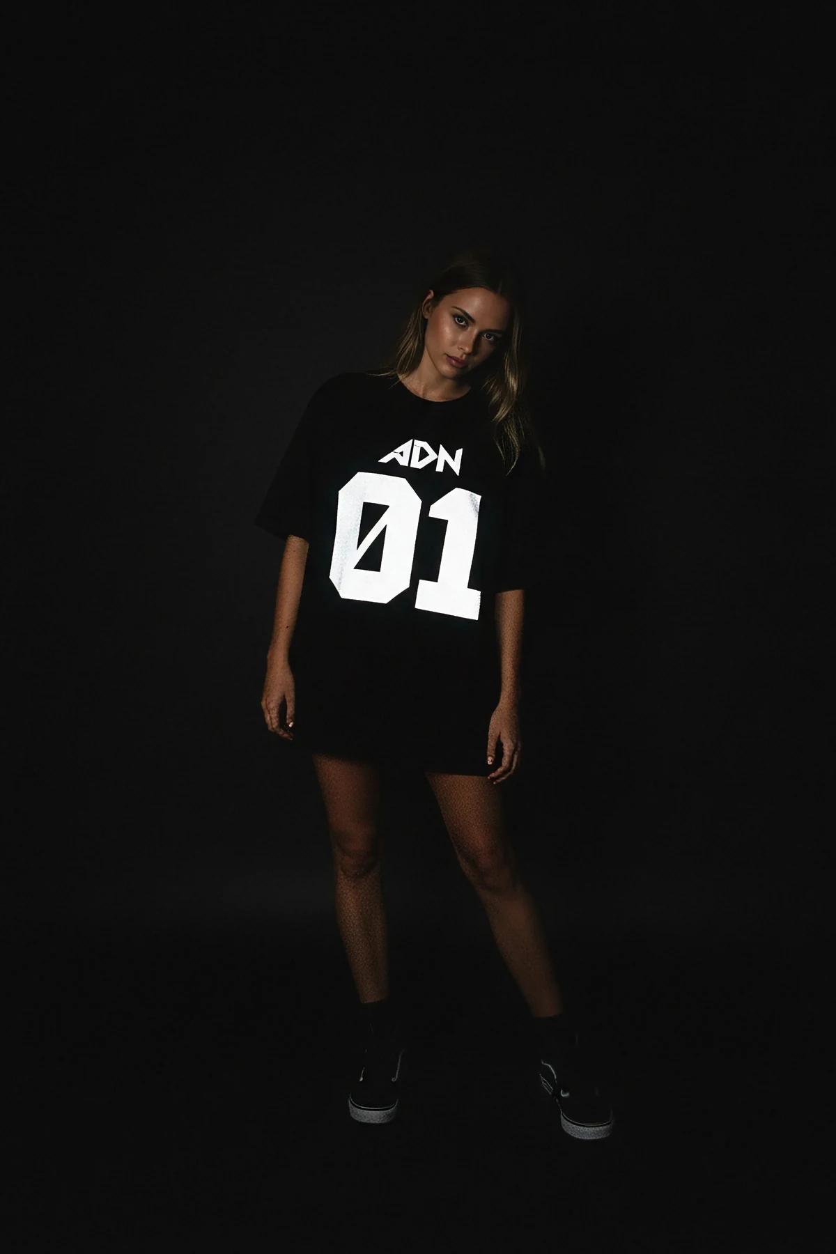 Black oversized t-shirt with white reflective 'ADN 01' graphic on front, worn by a woman.