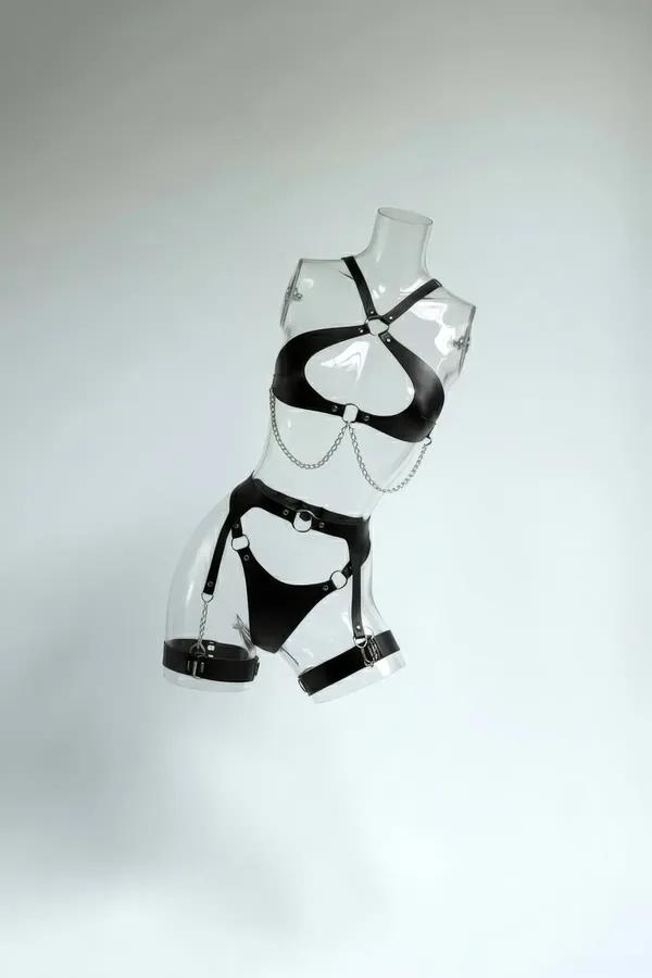 Full body harness in black faux leather featuring draped silver chest chains, garter straps, and matching leg bands