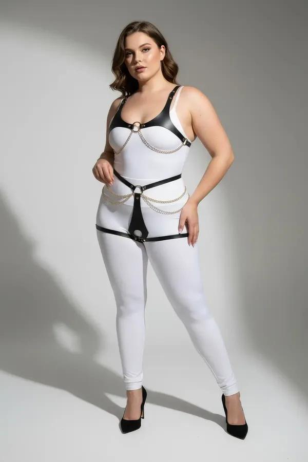 Black faux leather body harness with draped gold chains and O-rings worn over white bodysuit, full torso view