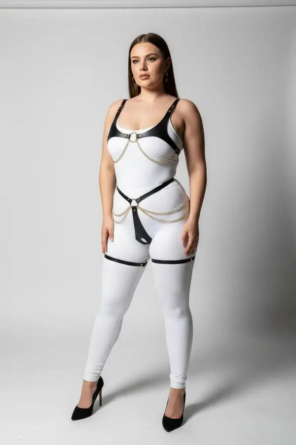 Black faux leather body harness with draped gold chains and O-rings worn over white bodysuit, full torso view