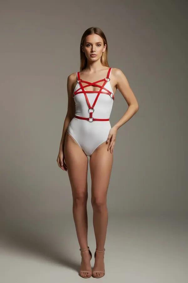 red faux leather cross-strap body harness with silver O-ring details at chest and waist, worn over white bodysuit