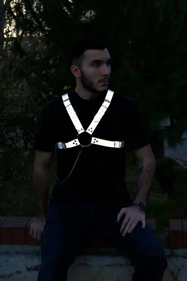 Reflektörlü gri erkek göğüs harness, ışık altında beyaz-gümüş parıltı, siyah O-ring ve metal zincir detayı