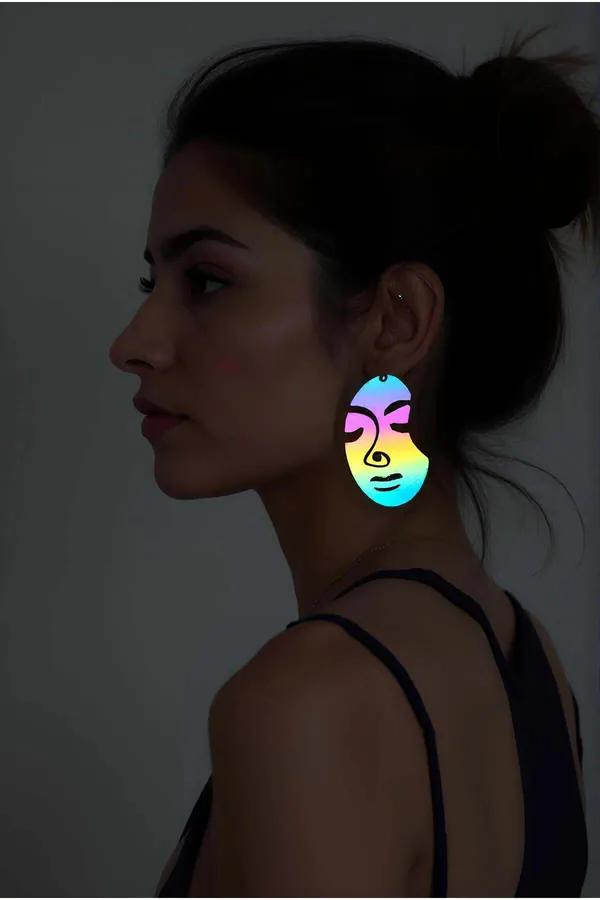 Rainbow reflective abstract face drop earring shown on model, iridescent cyan-to-yellow acrylic pendant with black line-art f