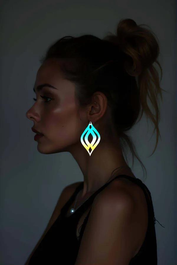 Iridescent cyan-to-yellow laser-cut drop earrings with nested flame-teardrop motif, silver hook, worn in profile against dark