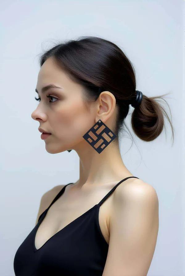 Matte black laser-cut geometric square earrings with rectangular cutout slot pattern worn on model ear, side profile view