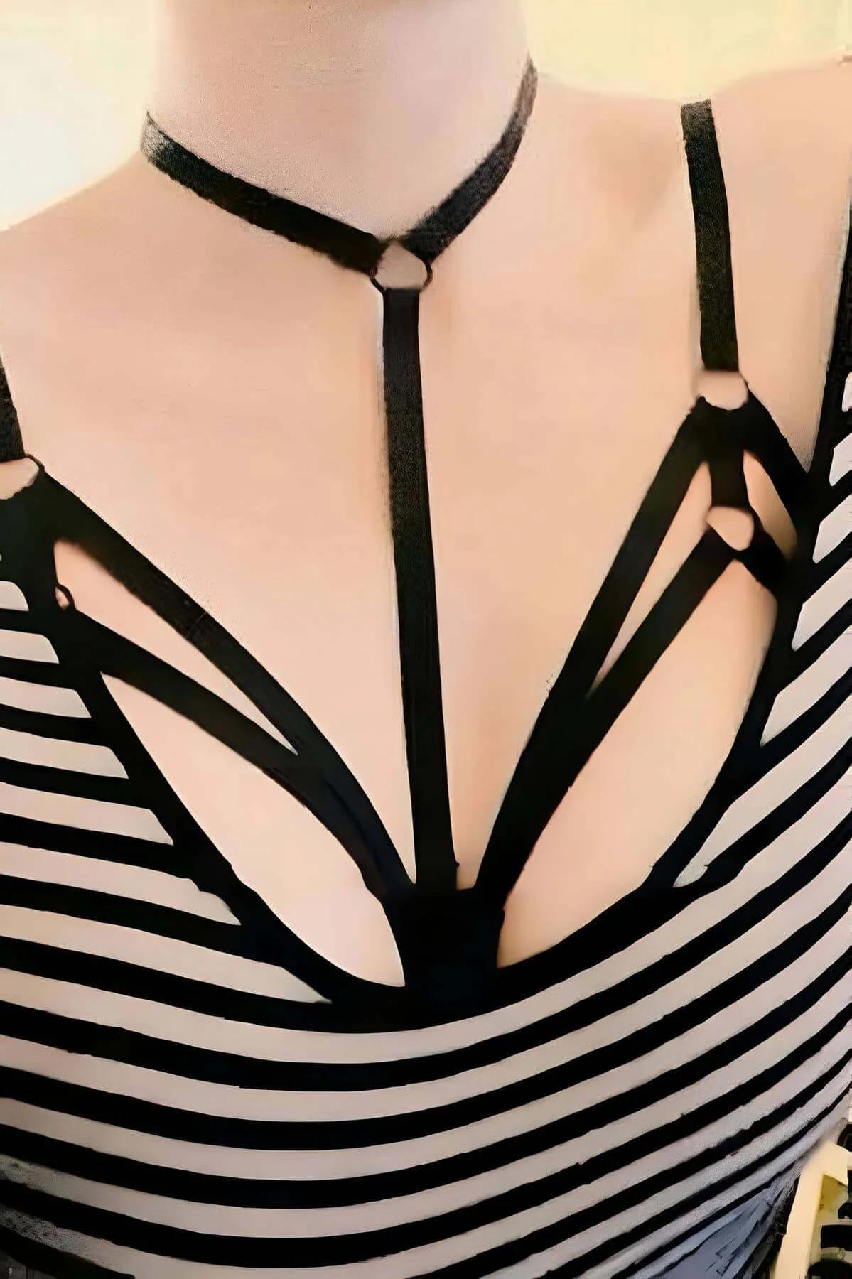 Black strappy chest harness with integrated choker and silver O-ring connectors worn over striped top