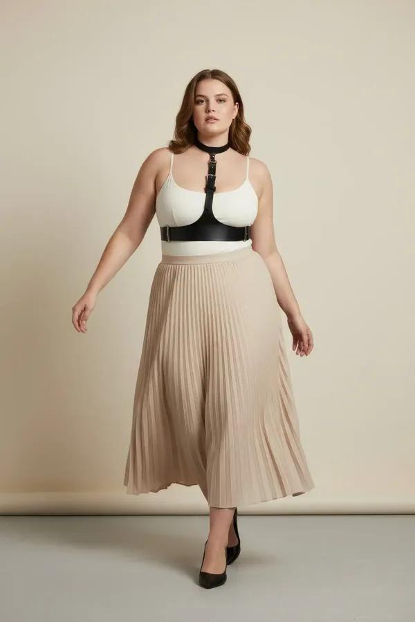 Black faux leather choker underbust harness with silver buckles worn over white bodysuit and beige pleated skirt