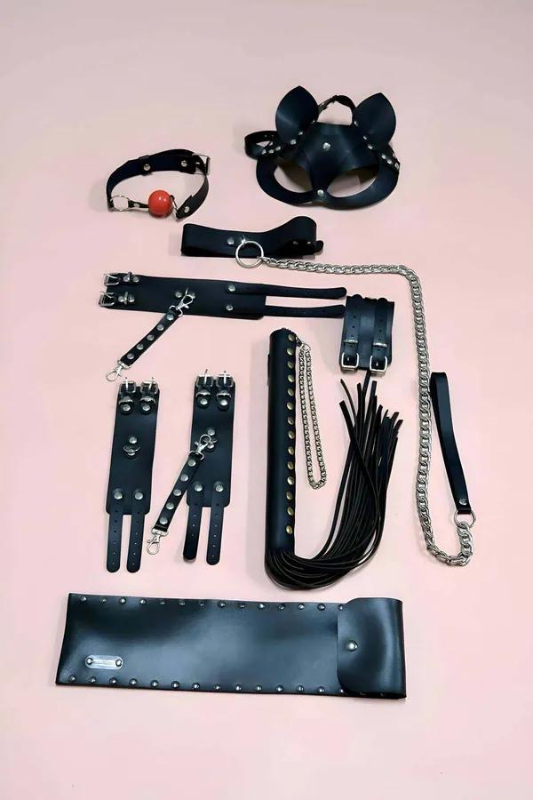 black vegan leather 7-piece accessory set with cat-ear mask, studded cuffs, flogger, silver chain and storage pouch on pink b