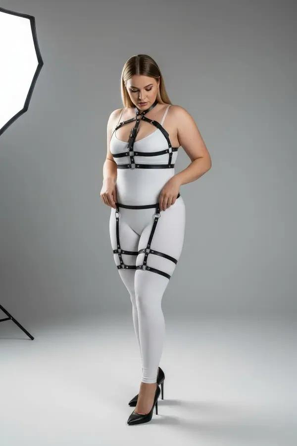Black faux leather full body harness with silver O-rings and double thigh garter straps worn over white bodysuit