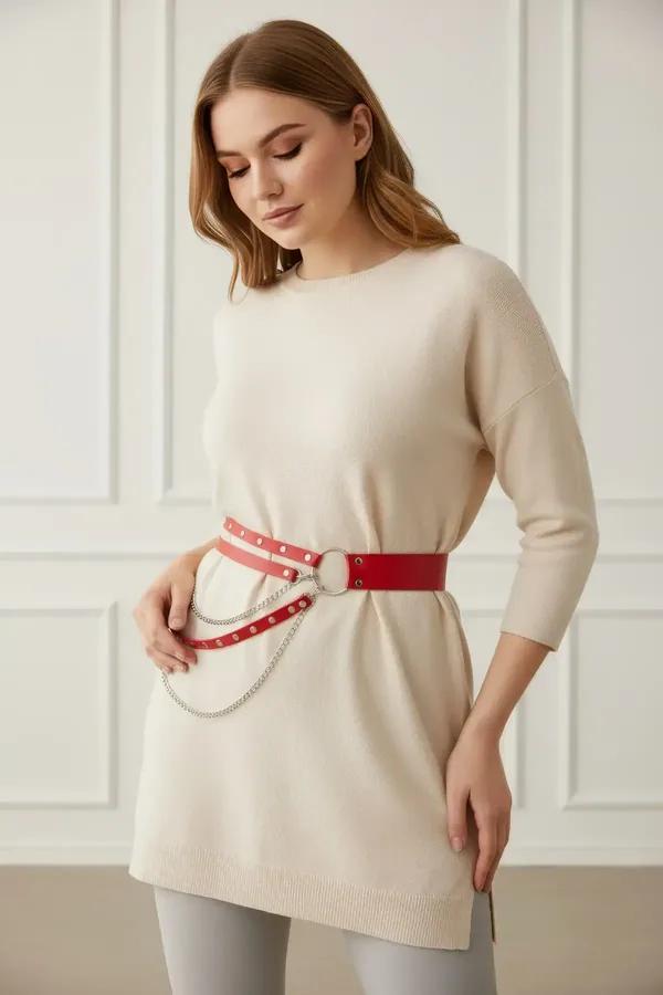 red faux leather waist harness belt with three draped silver chains worn over cream sweater and light blue jeans