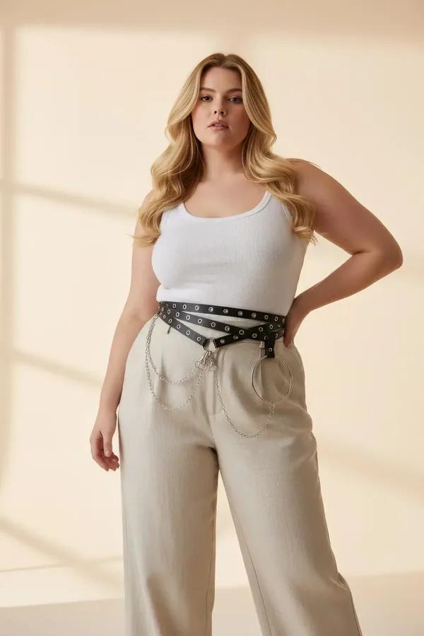 black faux leather waist harness with silver eyelet studs and O-ring with draped triple-strand chains worn over beige trouser
