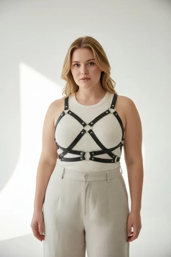 Black faux leather criss-cross body harness with silver O-rings and rivets worn over white ribbed top