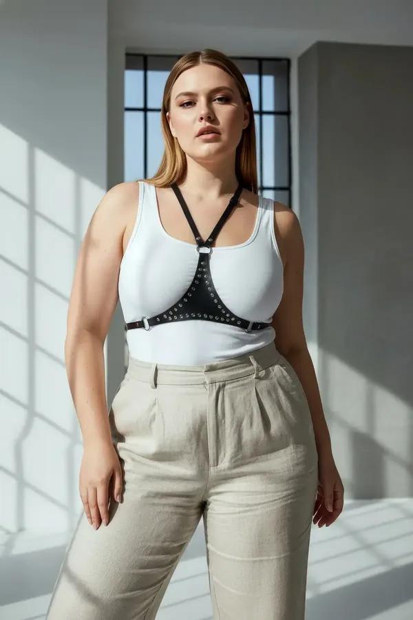 Black faux leather chest harness with silver metal studs and center O-ring, worn over white tank top