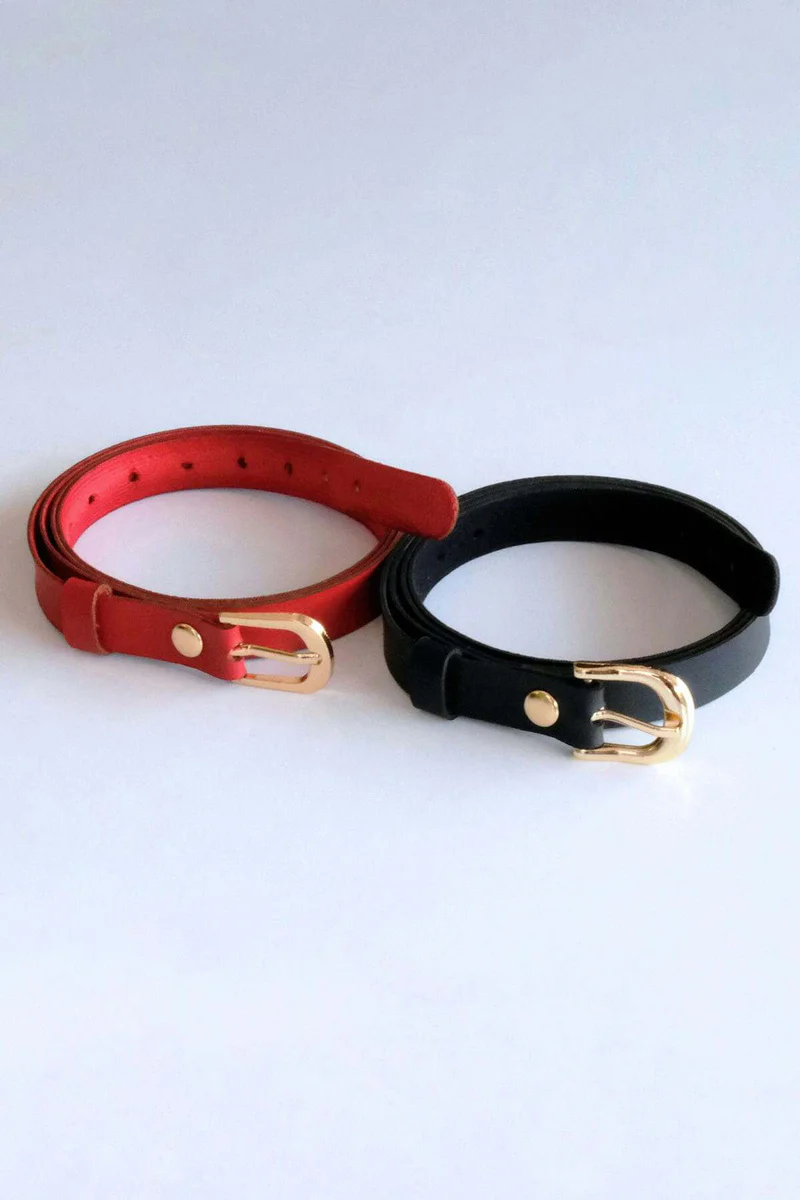 Slim black faux leather belt with buckle coiled, next to a red faux leather belt with buckle coiled.